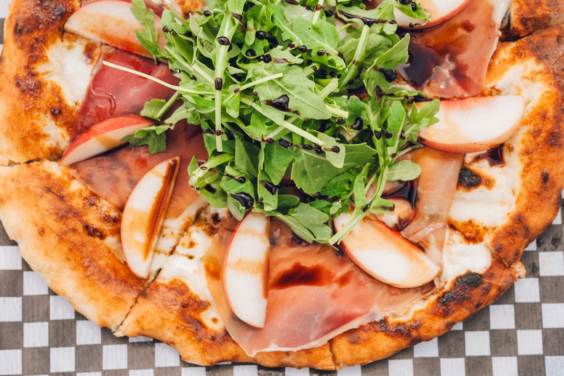 Pizza with peaches and arugula on top of it.